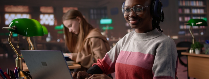 African girl comparing course notes with data from library collection, using laptop to focus on a literature assignment. Young student working on her diploma project. Camera B.