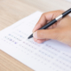 Closeup of hand holding pen and filling out questionary form on table