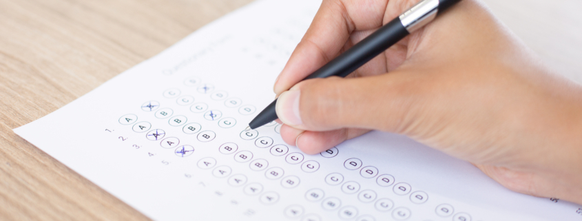 Closeup of hand holding pen and filling out questionary form on table