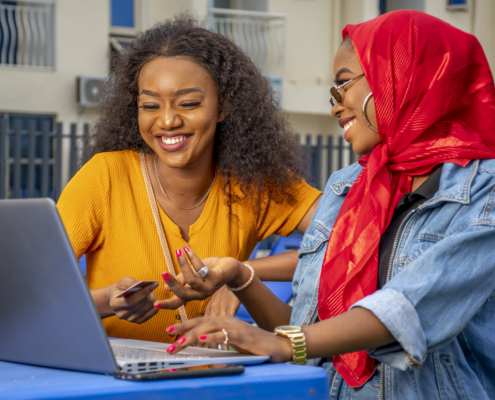 A closeup shot of two cheerful young African ladies and a laptop