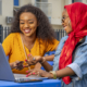 A closeup shot of two cheerful young African ladies and a laptop