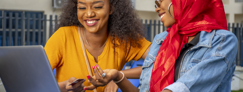 A closeup shot of two cheerful young African ladies and a laptop