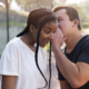 guy whispering something surprising into the african girl's ear and she looks very surprised