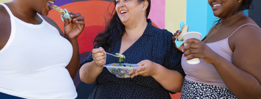 three moms together eating and laughing together standing outdoors
