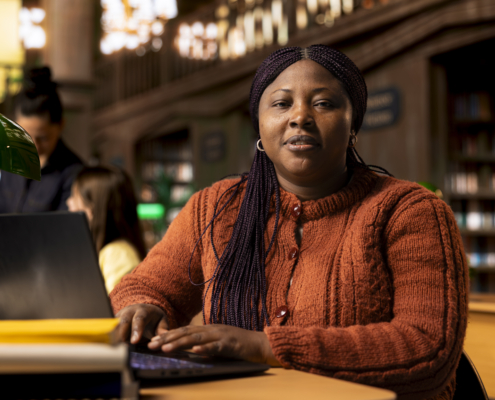 Portrait of african teacher working with academic resources and learning materials within the public library database. Smiling woman focused on her educational profession.