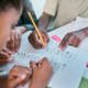 School, children and hands writing for teamwork with learning activity in classroom group together. Young kids and students working on literacy and academic exercises for development at desk