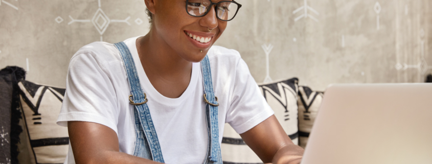 Stylish businesswoman works on laptop computer in cozy coffee shop, keyboards information, messages in social networks, has happy expression, wears glasses for good vision, focused into monitor