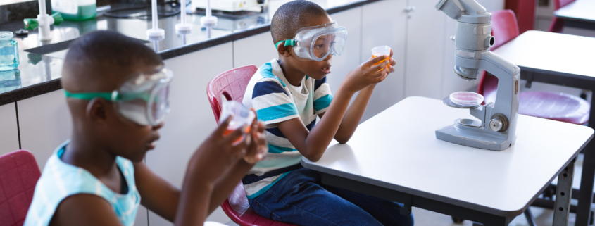 Two african american boys wearing protective glasses holding a beaker in science class at laboratory. school and education concept