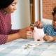 A woman and child saving money in a piggy bank. Coins and bills on the table. Teaching financial responsibility and saving habits. Family financial education. African family at home.